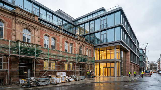 Zwei Personen sitzen in einem modernen Coworking Space an jeweils einem Tisch und arbeiten am Laptop..
